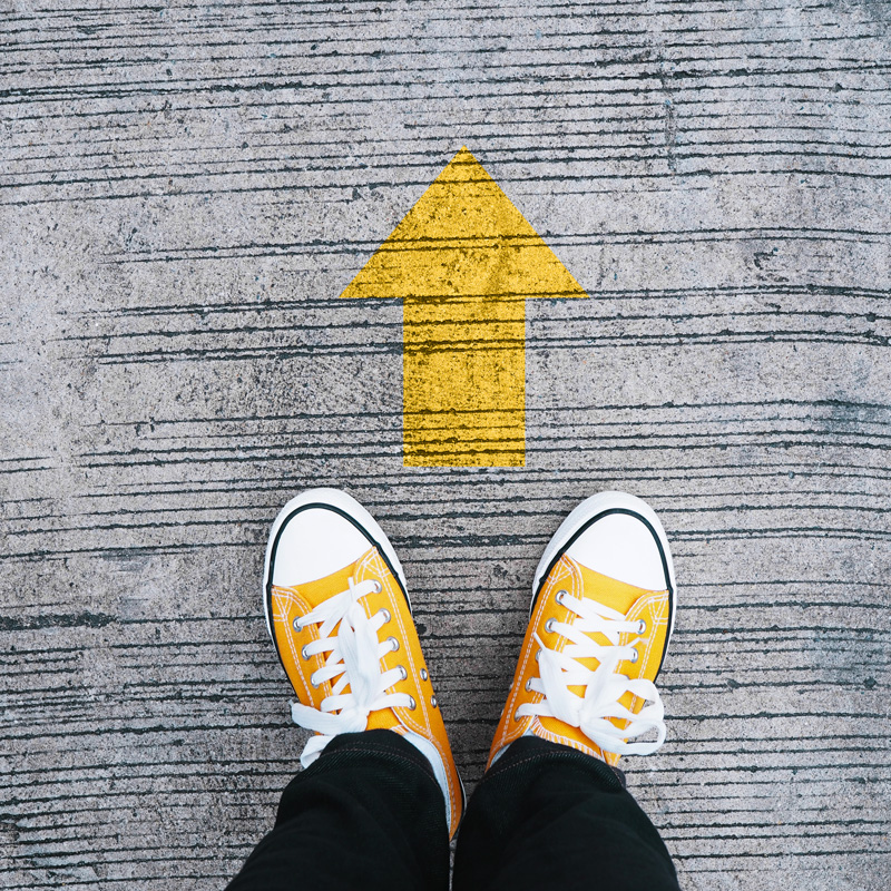 Photo of a pair of yellow canvas sneakers and a yellow arrow on the ground pointing forwards